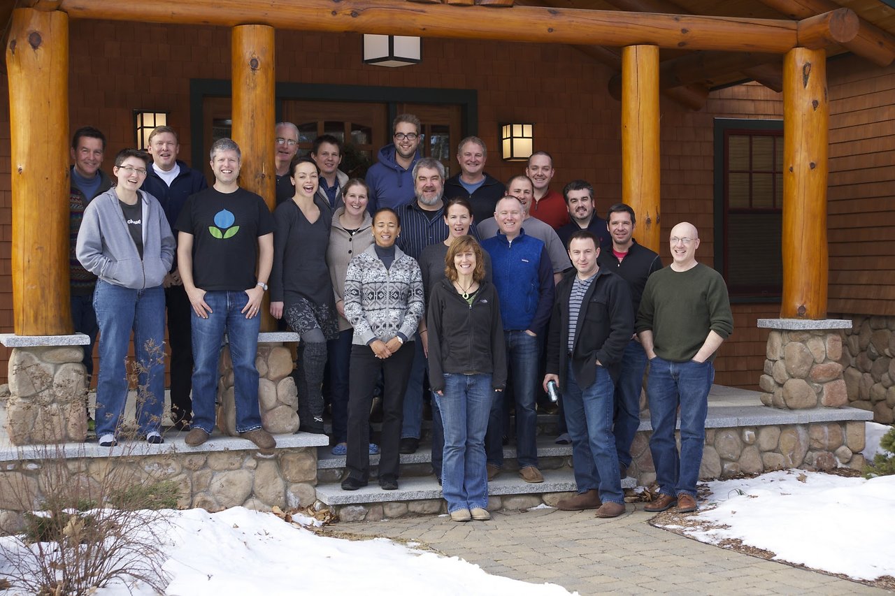 A group of people posing together on the steps of a wooden lodge, smiling at the camera.