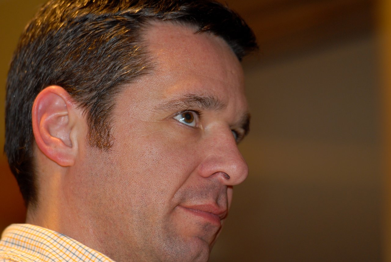 Close-up of a man looking to the side with a neutral expression in an indoor setting.
