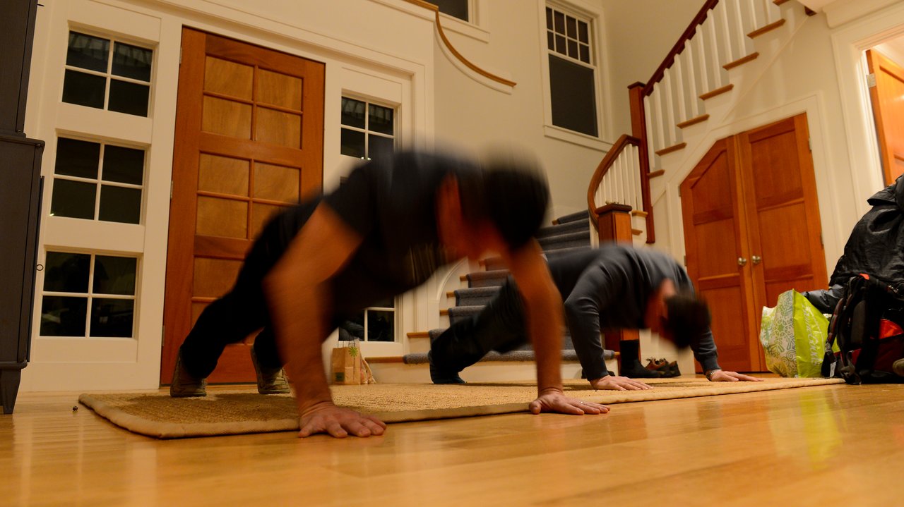 Two people doing push-ups on a rug in a home setting, captured with motion blur.