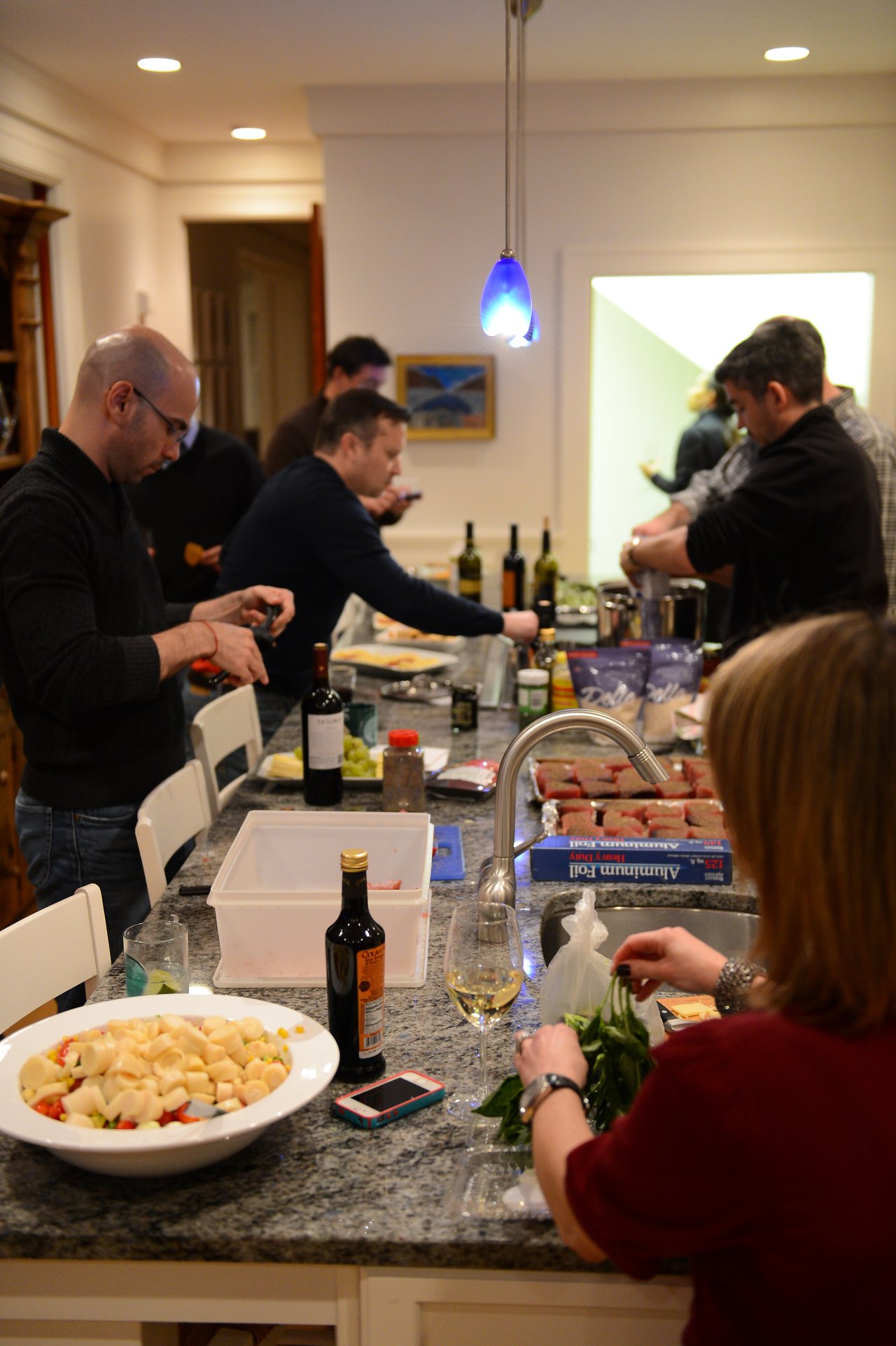 A group of people prepares food together in a kitchen, chopping ingredients and arranging items on the counter.