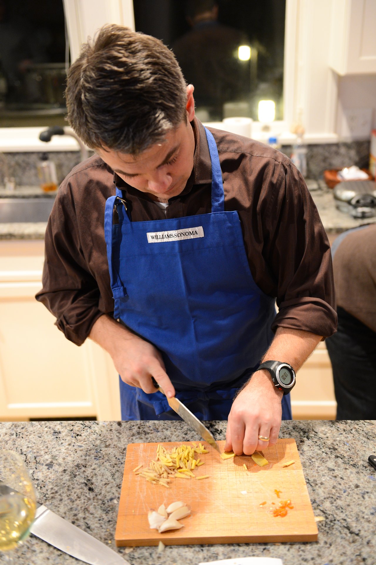 A person wearing a blue apron chops ingredients on a cutting board in a kitchen.