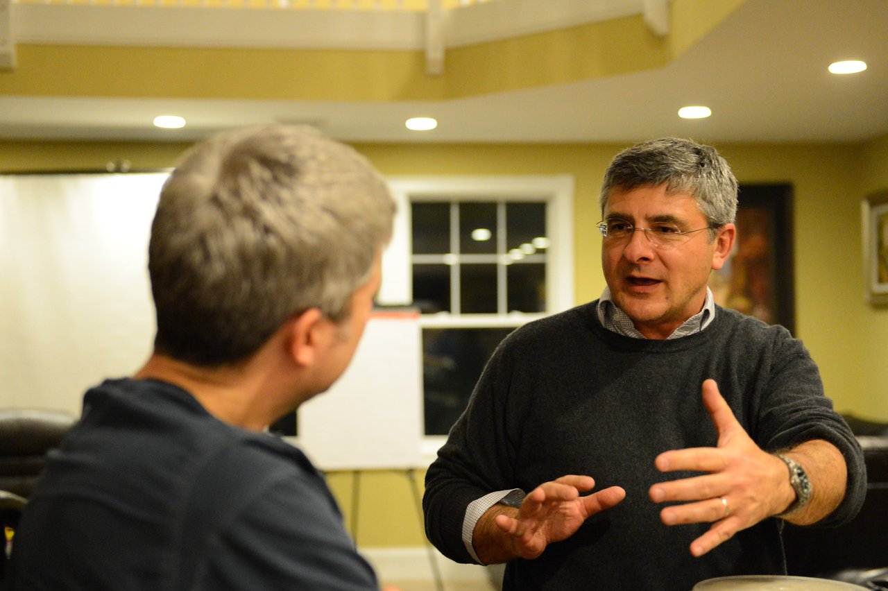Two men engaged in conversation, one gesturing with his hands while the other listens attentively.
