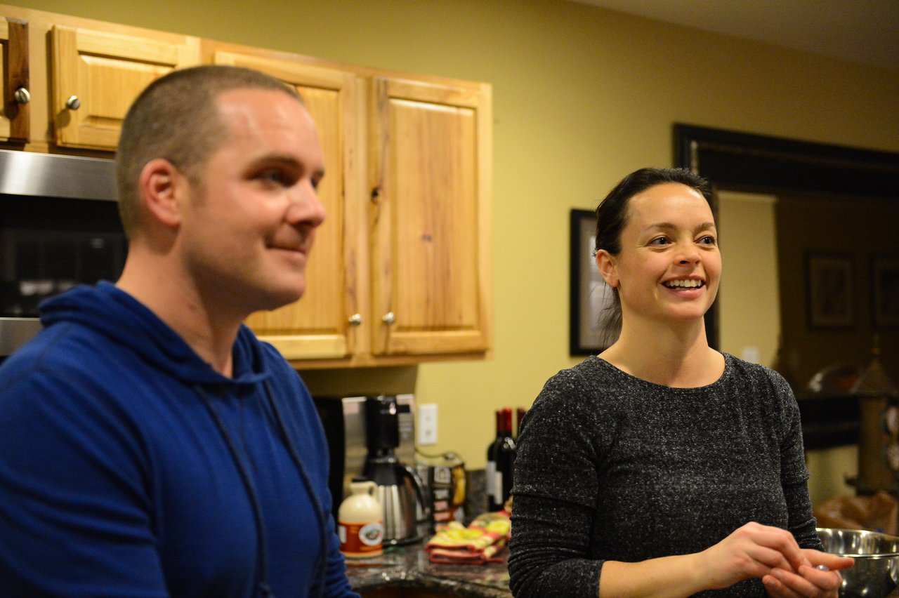 Two people in a kitchen, one smiling and speaking while the other listens.
