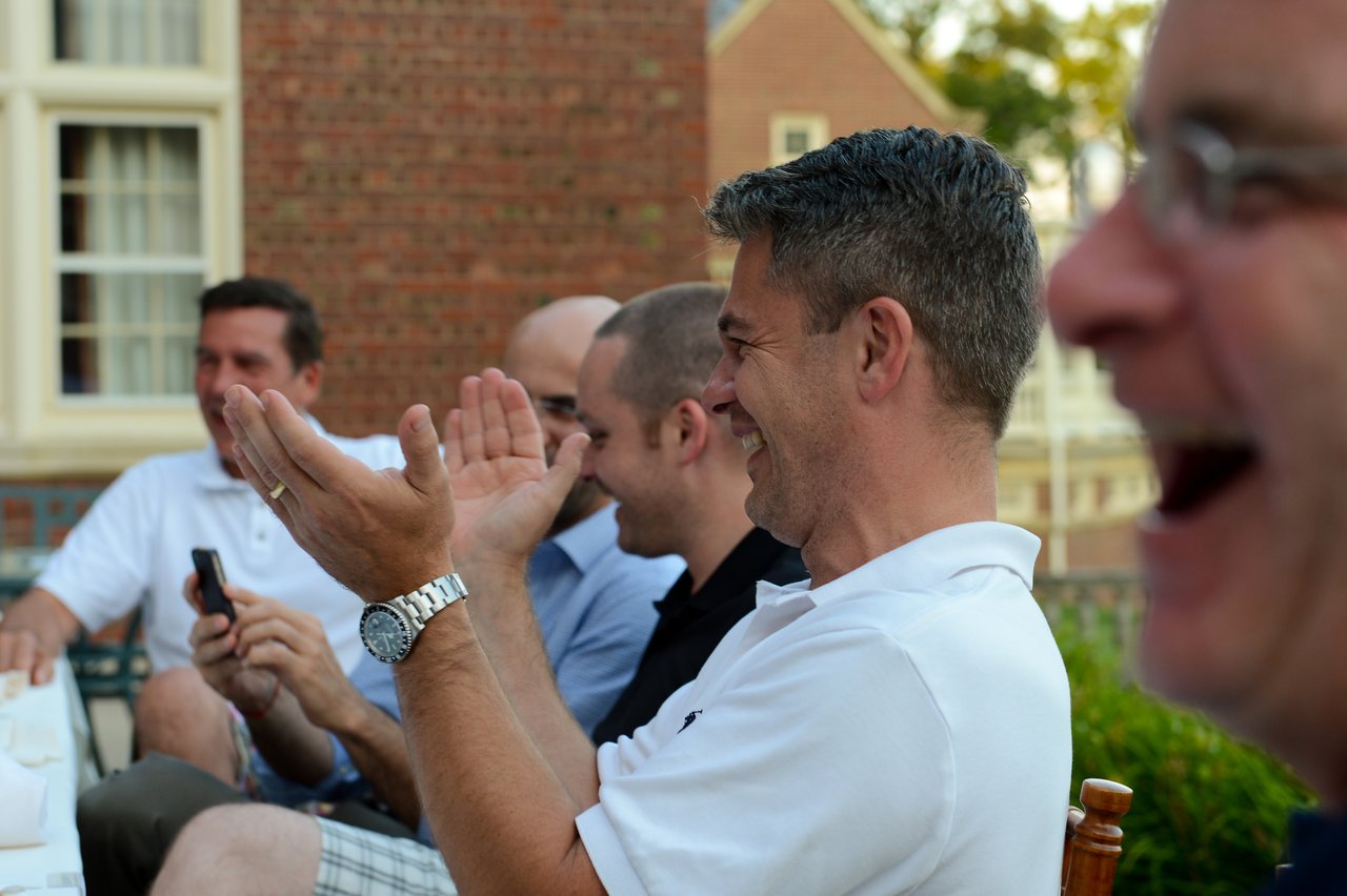 A group of people at an outdoor dinner, laughing and clapping while enjoying a conversation.