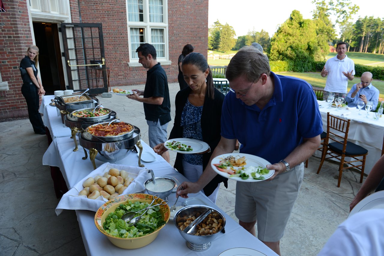 People serving themselves food from a buffet table at an outdoor dinner event.