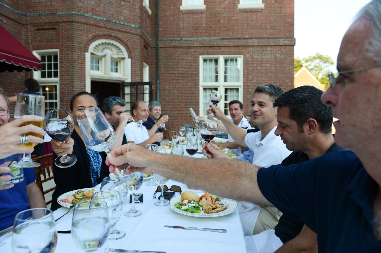 A group of people raising glasses in a toast during an outdoor dinner at a long table.