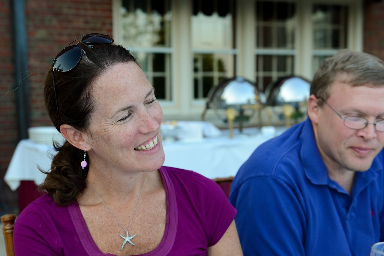 A woman in a purple shirt smiles while sitting next to a man in a blue shirt at dinner.