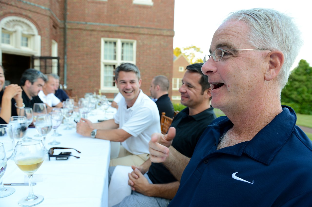 A group of people sits at a long table outdoors, engaged in conversation and laughter during dinner.