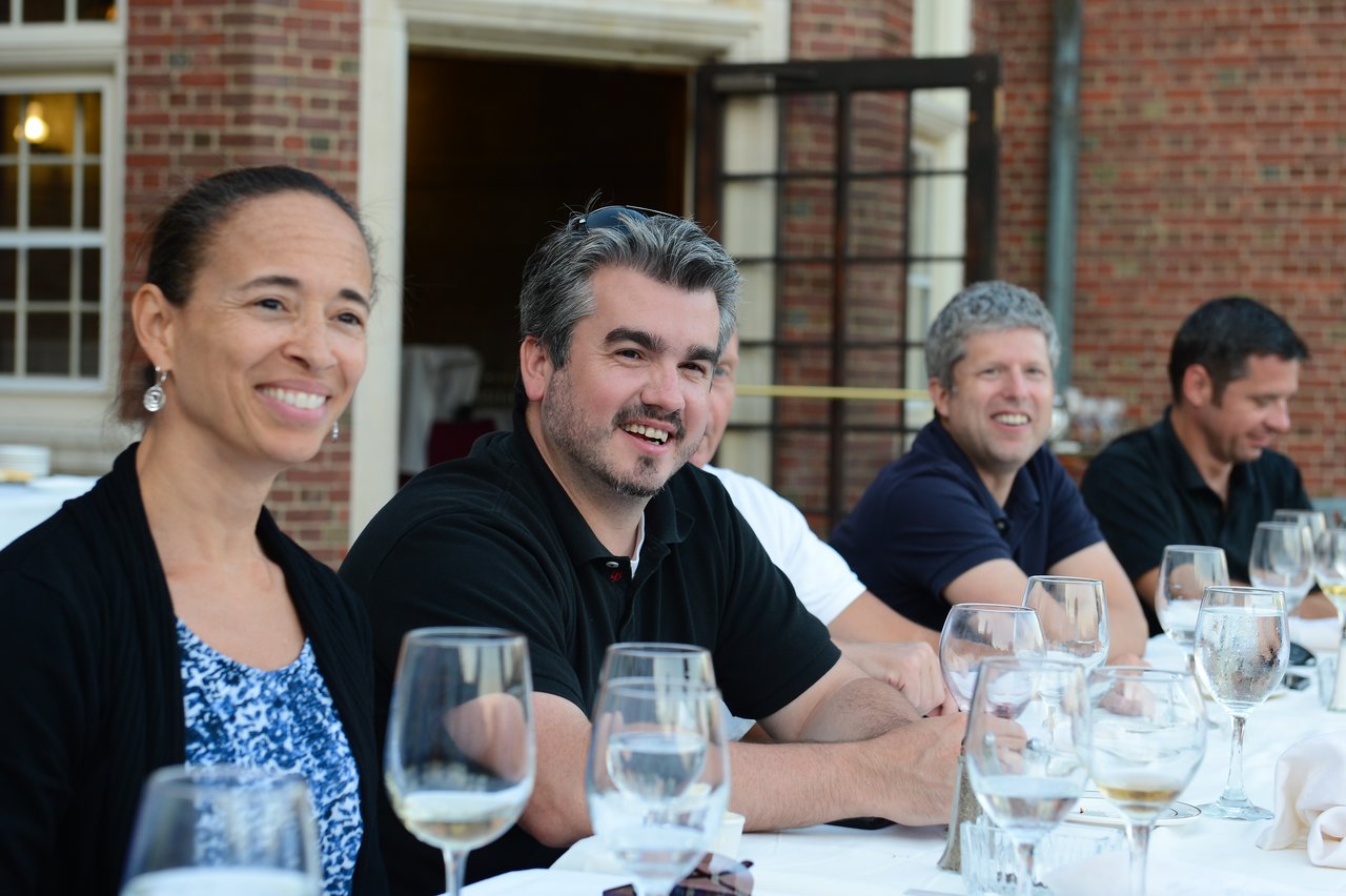 A group of people sitting at a dinner table, smiling and enjoying conversation with drinks in front of them.