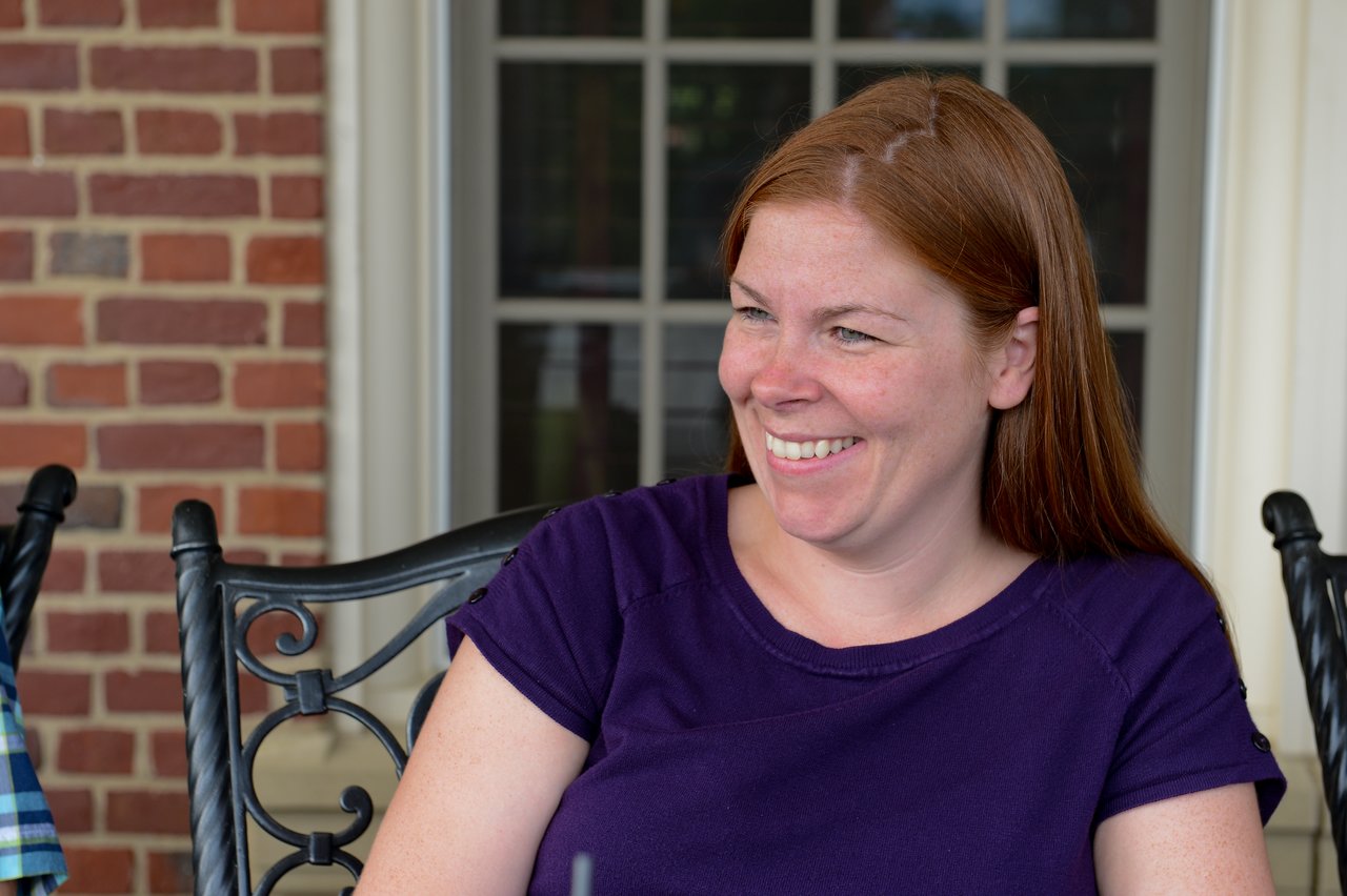 A woman in a purple shirt sits outside, smiling while engaged in conversation.