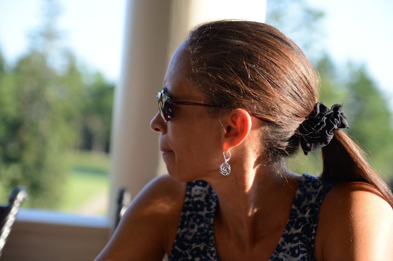 A woman wearing sunglasses and a patterned top sits outdoors, looking to the side.