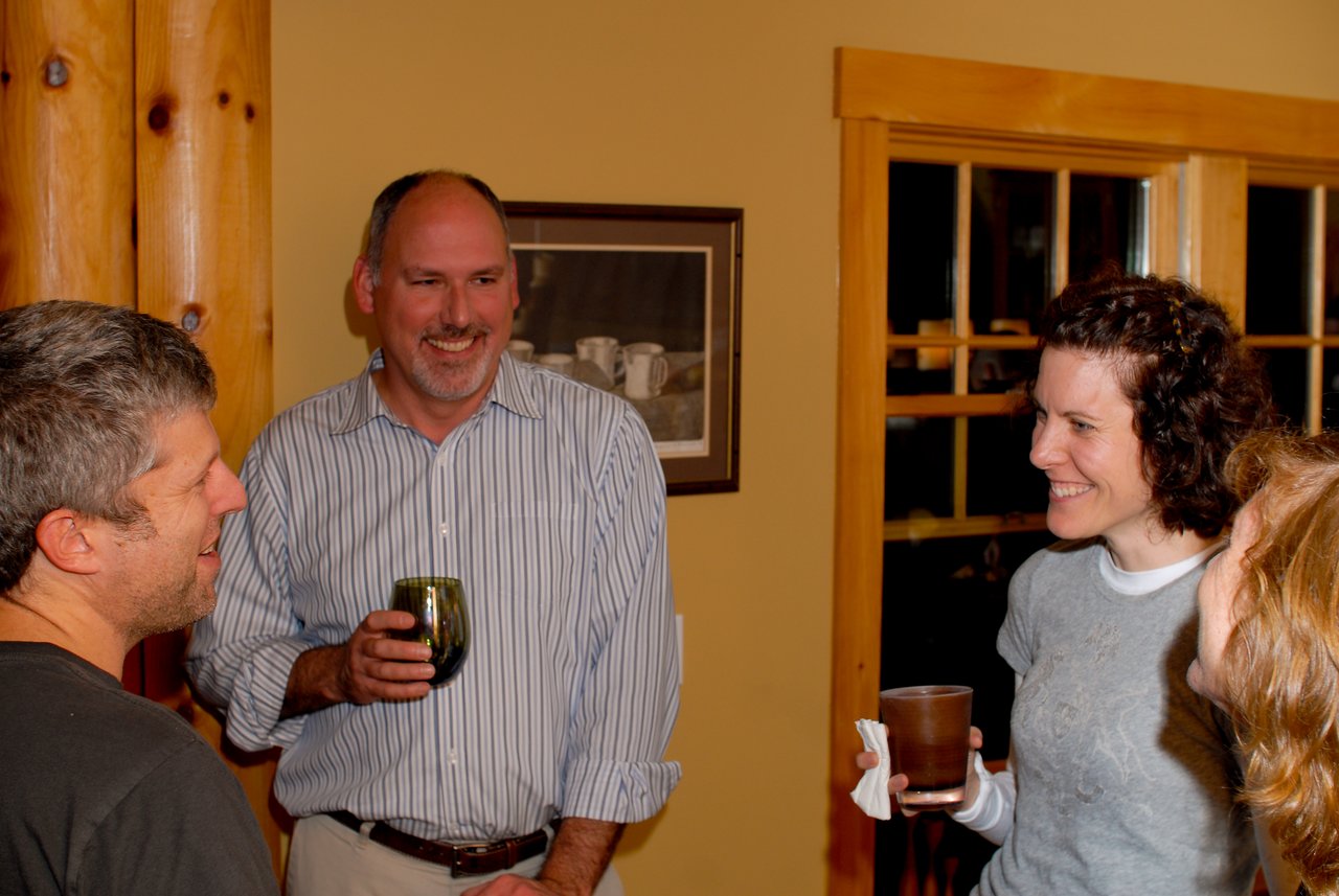 A group of people smiling and chatting indoors, holding drinks in a relaxed setting.