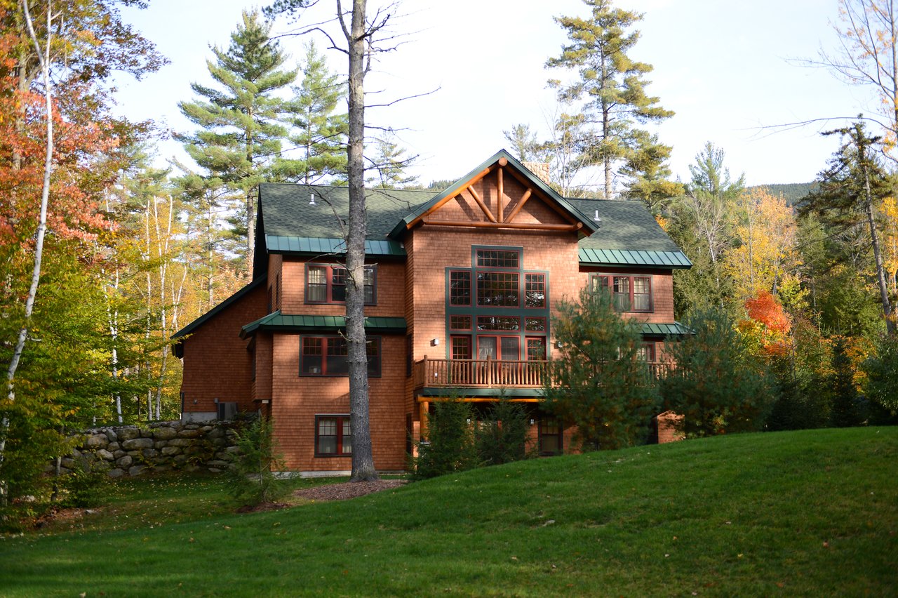 A large wooden house with green roofs surrounded by trees and grass, taken during daytime in autumn.