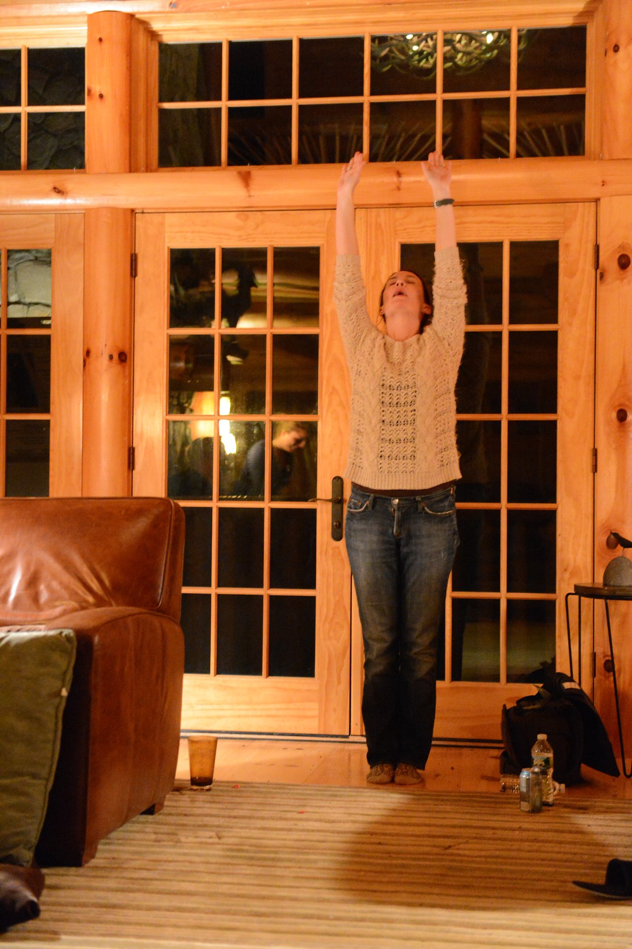 A person stands indoors with arms raised, looking up.