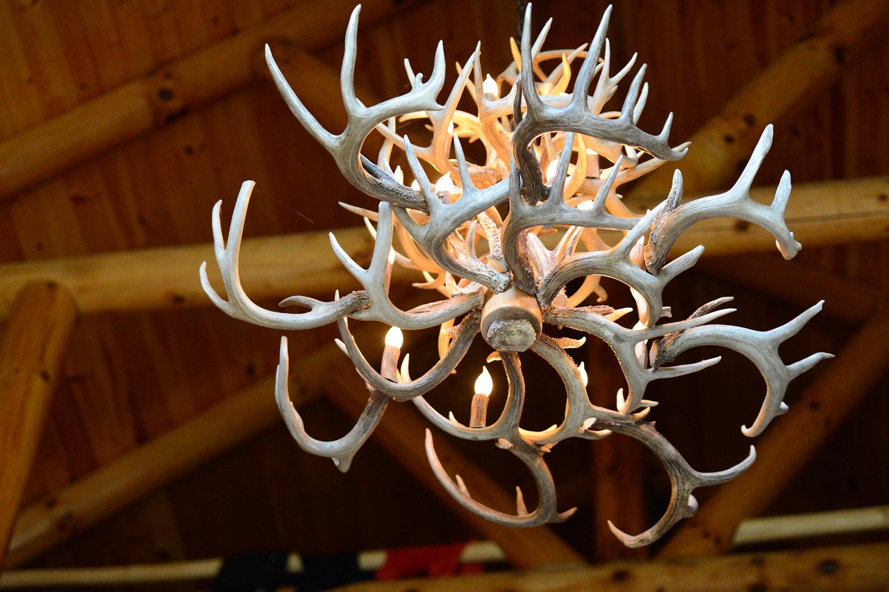 A chandelier made of antlers with glowing light bulbs hangs from a wooden ceiling.