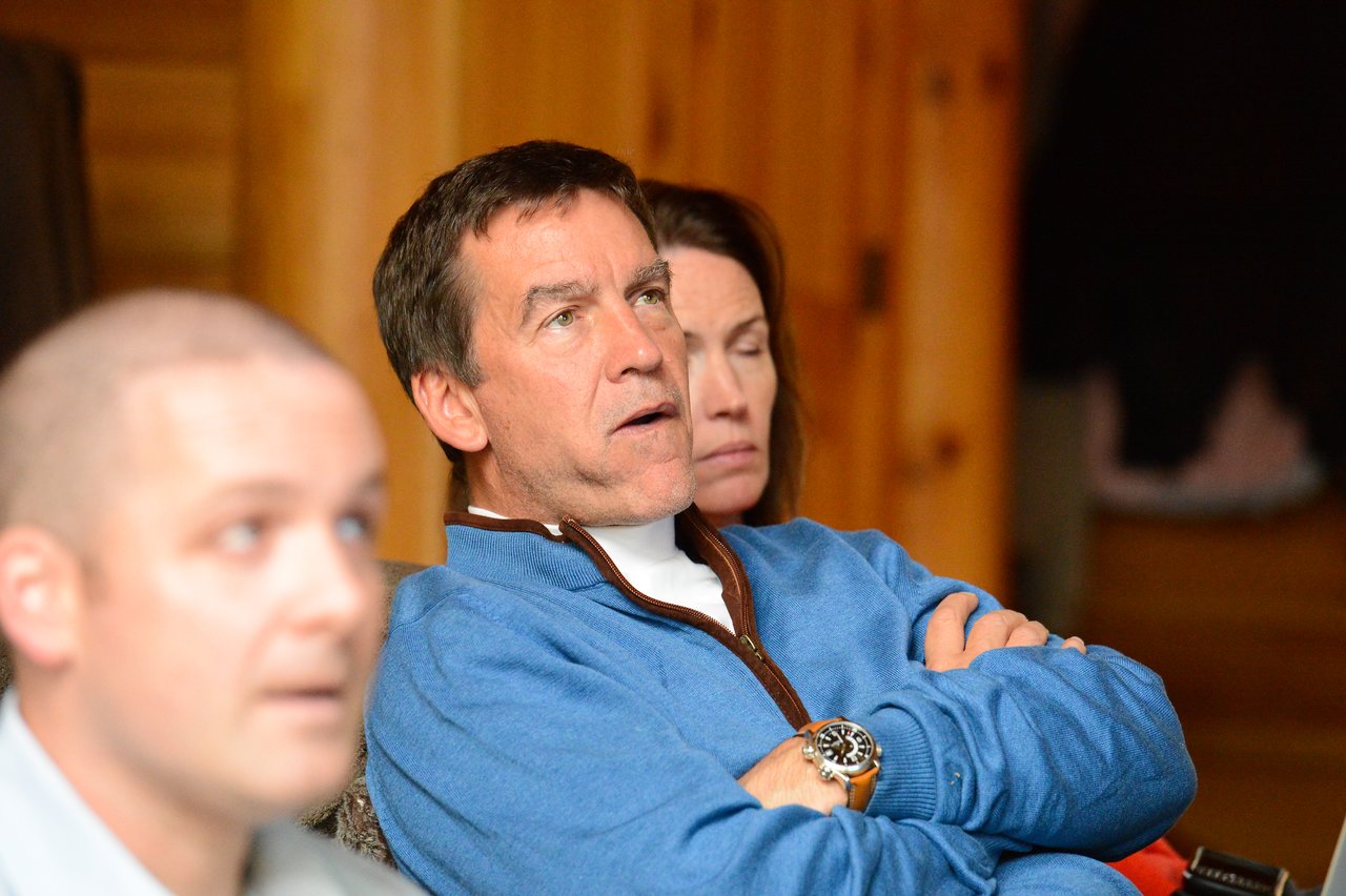 Three people sit indoors, appearing focused.