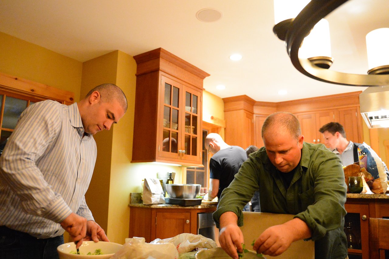 Several people prepare food in a kitchen, chopping ingredients and mixing in bowls.