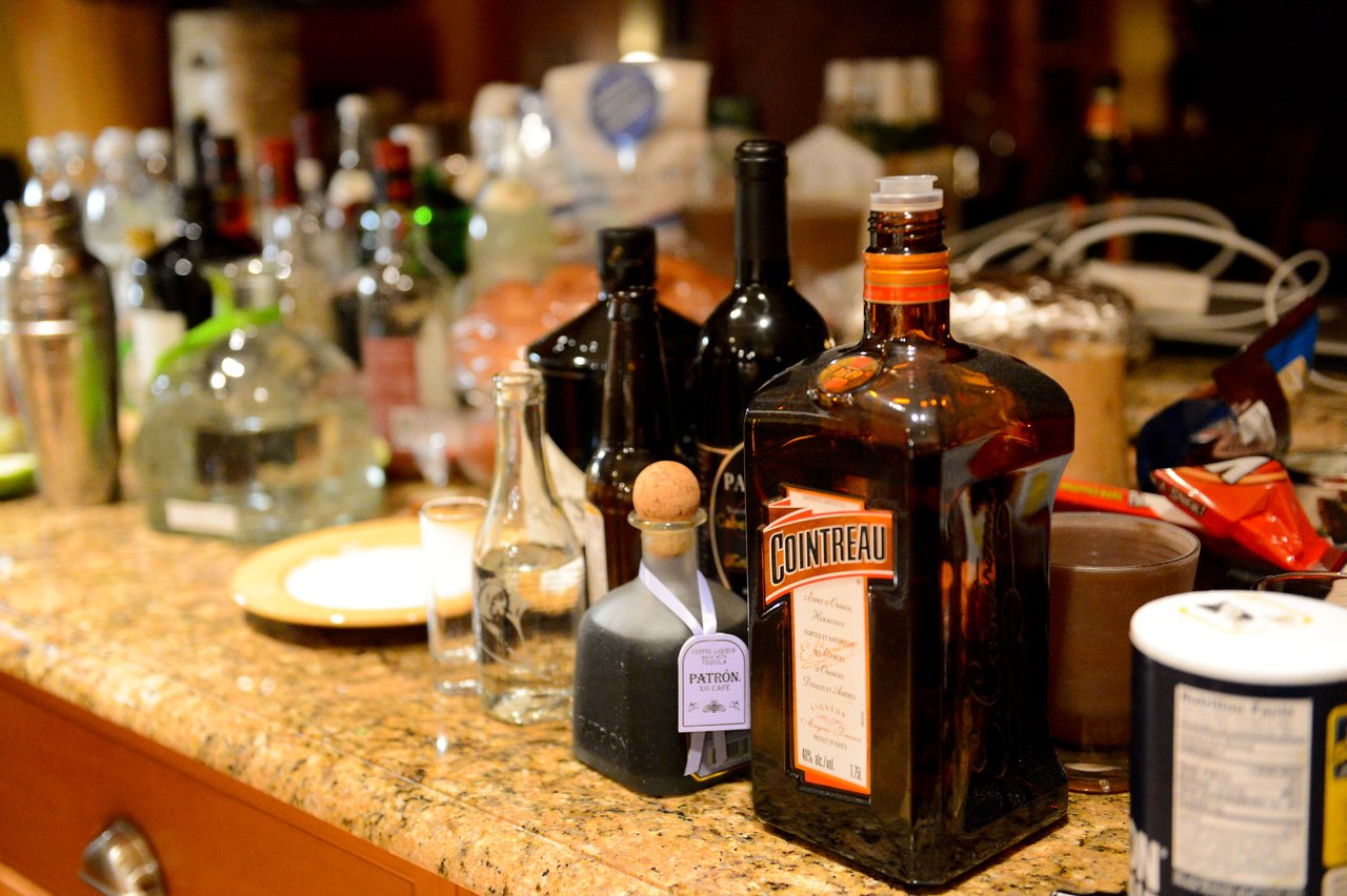 A countertop filled with various liquor bottles, shot glasses, and snacks at a gathering.