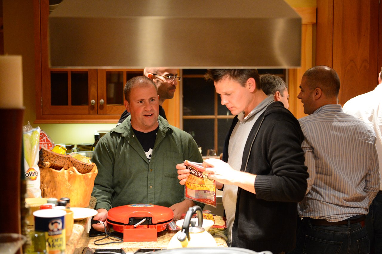 Several people gather in a kitchen, preparing food and talking.