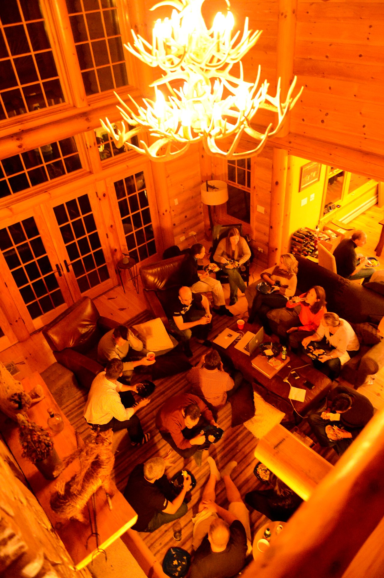A group of people gathers in a cozy cabin, sitting on couches and the floor, eating and talking.