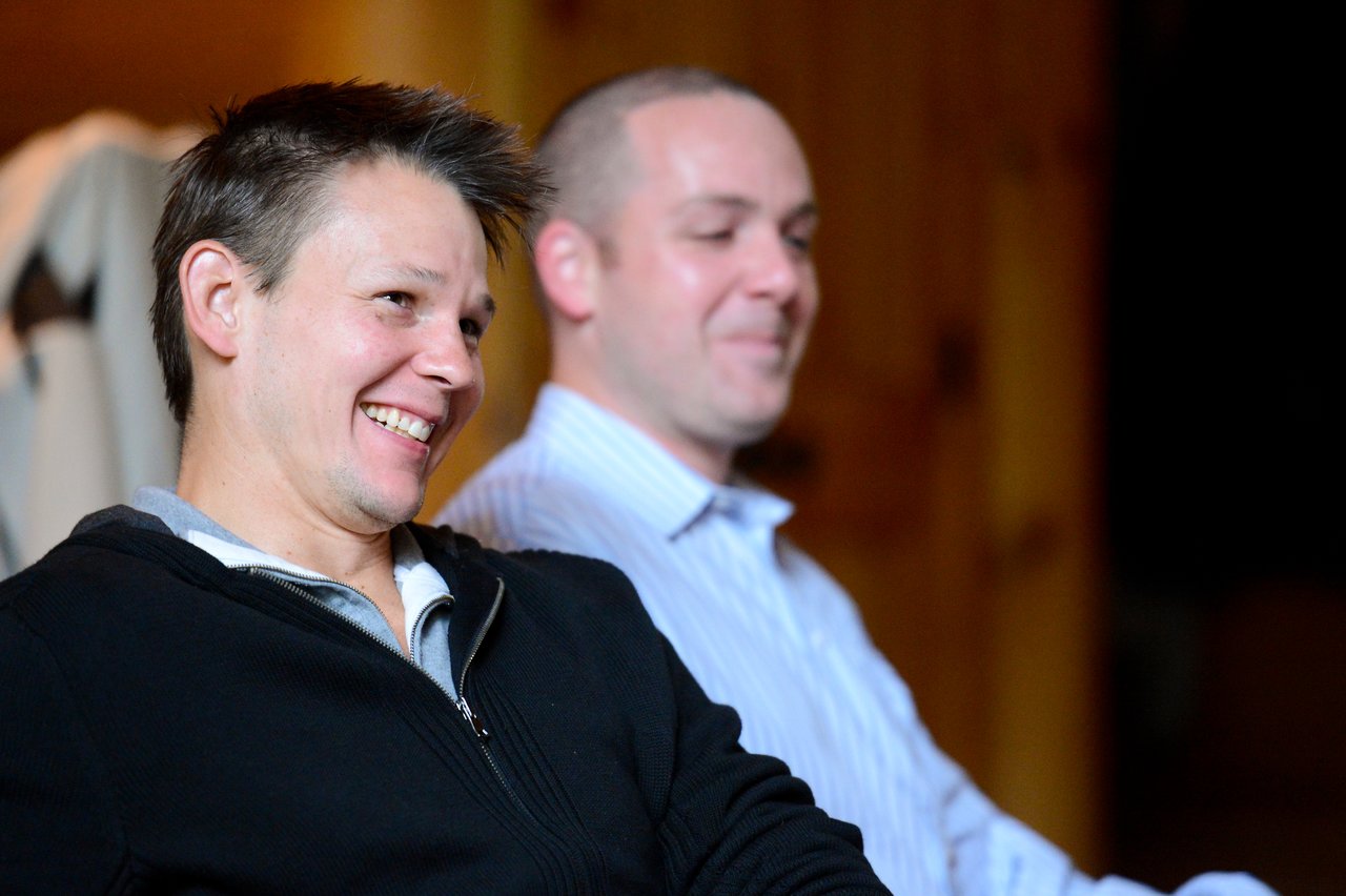 Two people sitting indoors, smiling and engaged in conversation.