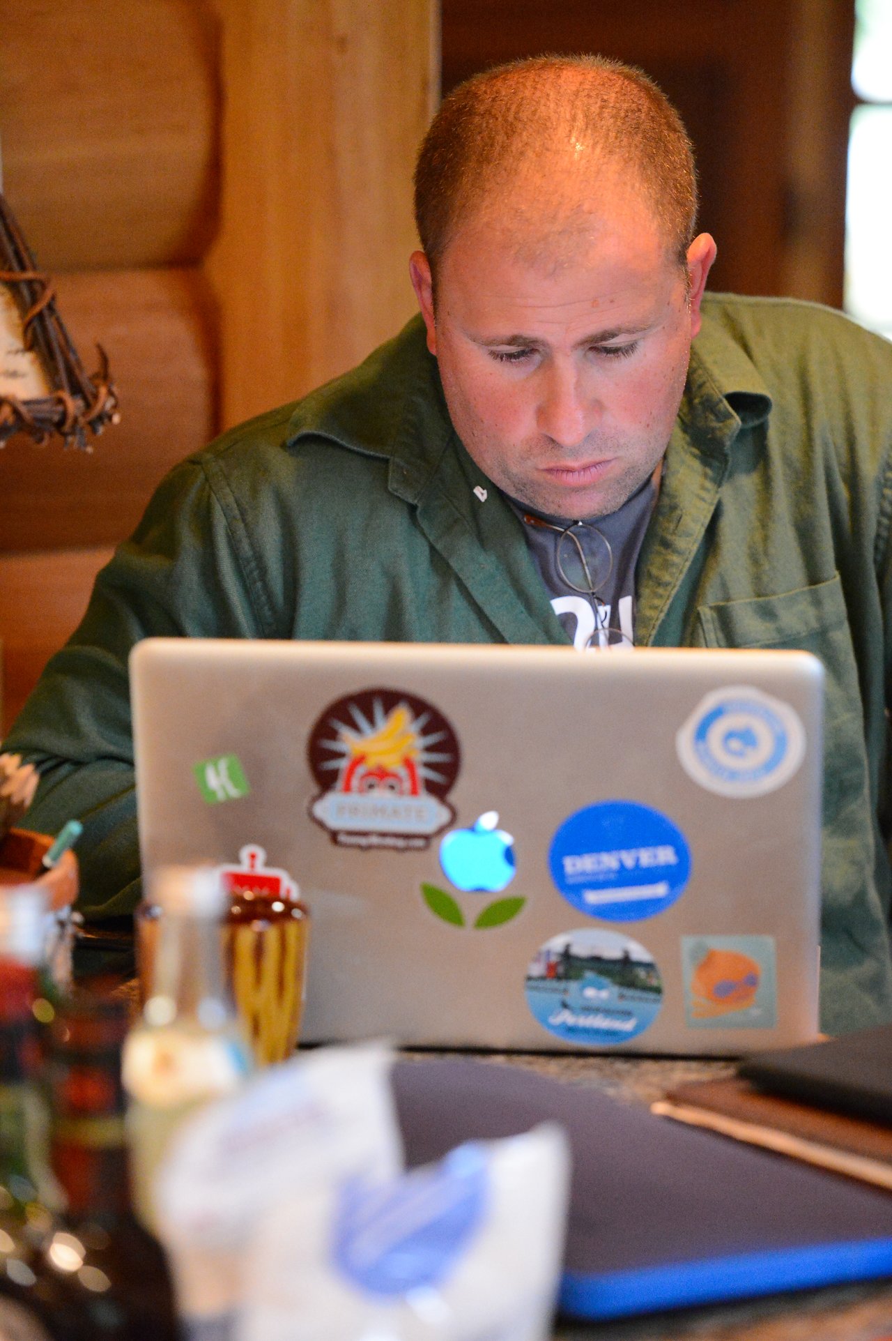 A person in a green shirt focuses on a laptop covered in stickers while working at a table.