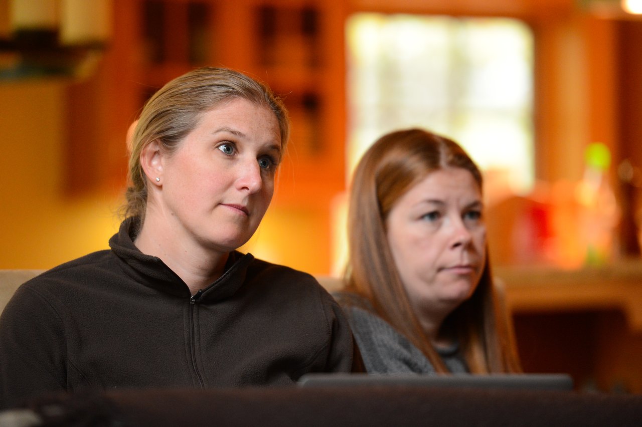 Two women sitting indoors, attentively listening to something off-camera with focused expressions.