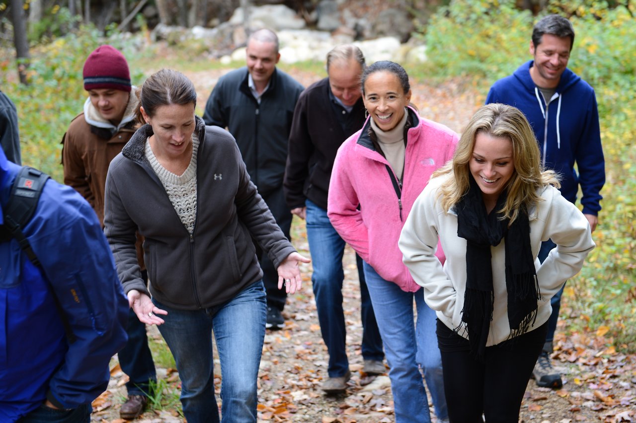 A group of people walks up a forest trail, smiling and talking during an outdoor team outing.