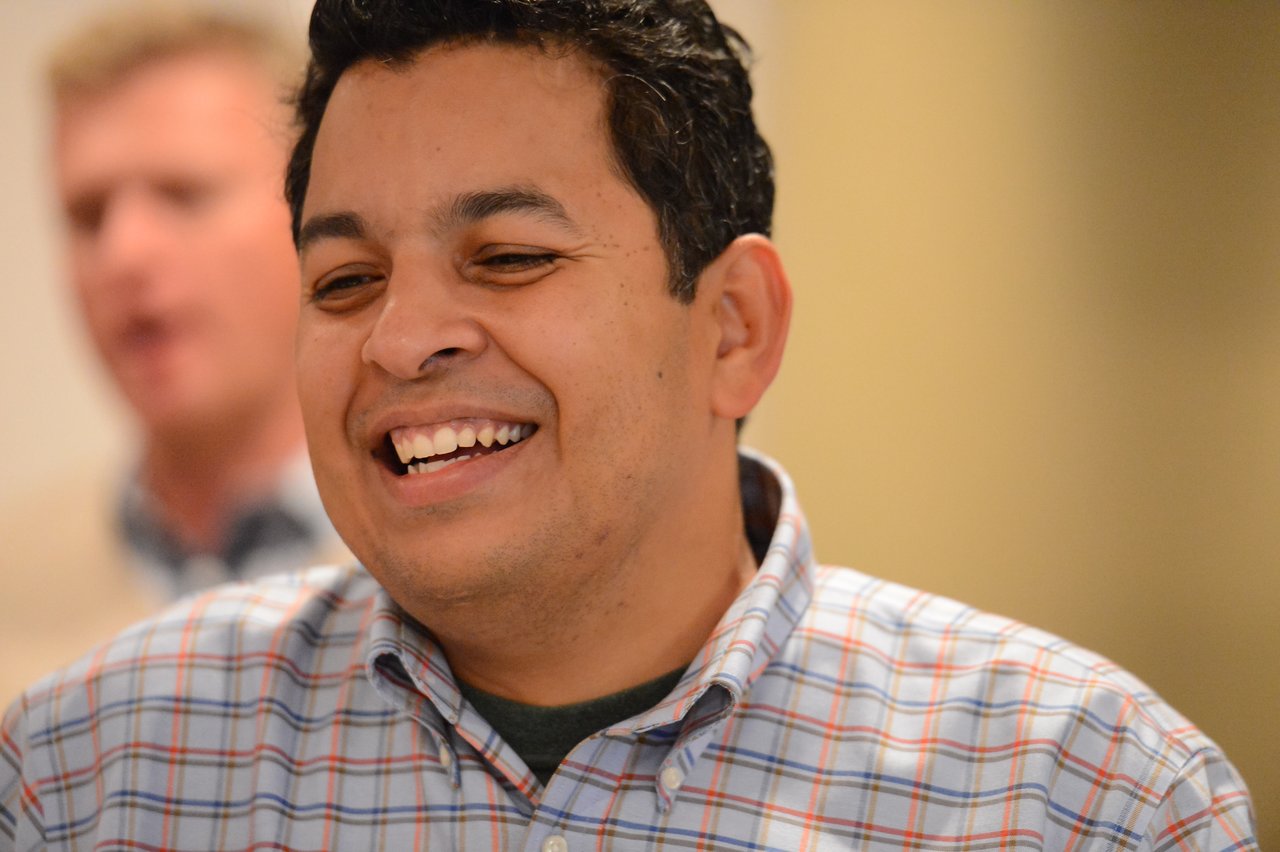 A man in a plaid shirt smiles while engaged in conversation at an Acquia offsite event.