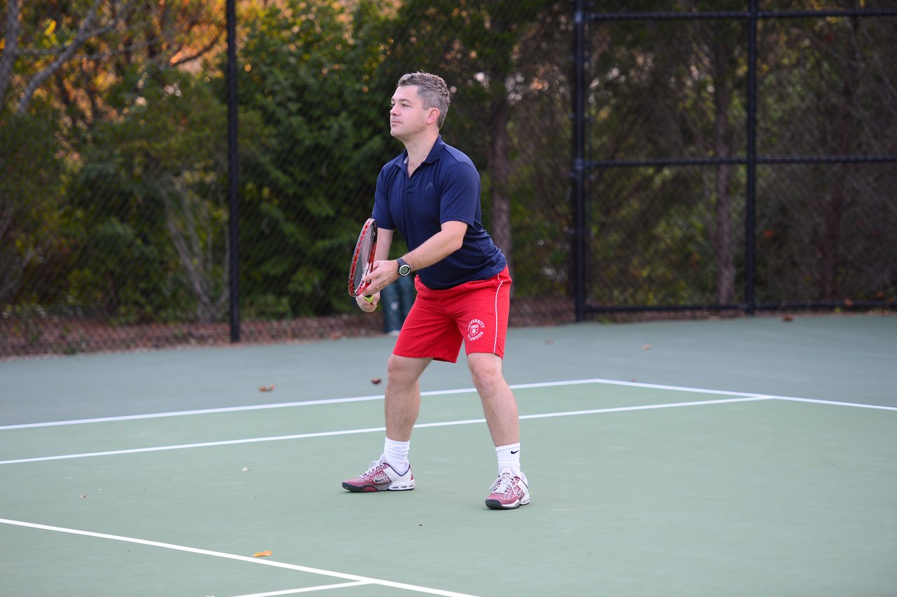 A man in sportswear holds a tennis racket and prepares to play on an outdoor court.