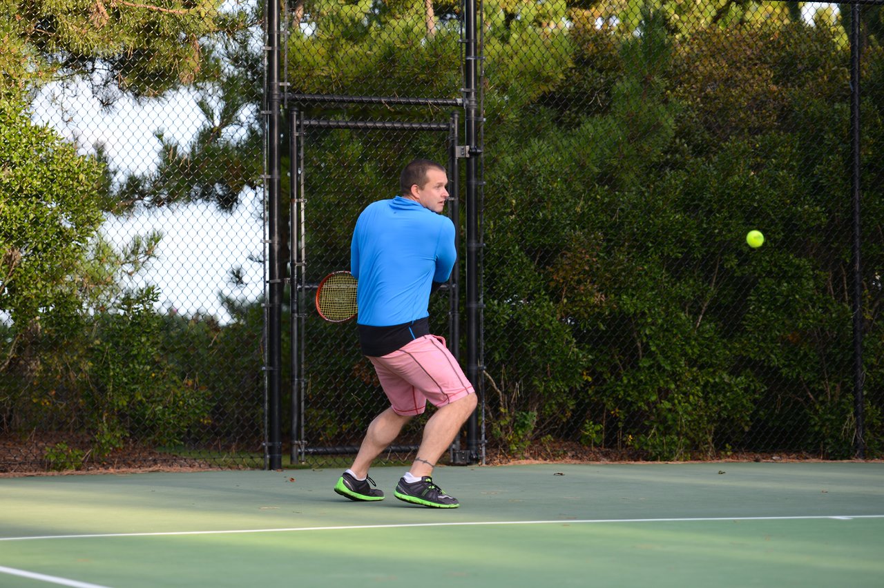 A man in sportswear prepares to hit a tennis ball with a backhand swing on an outdoor court.