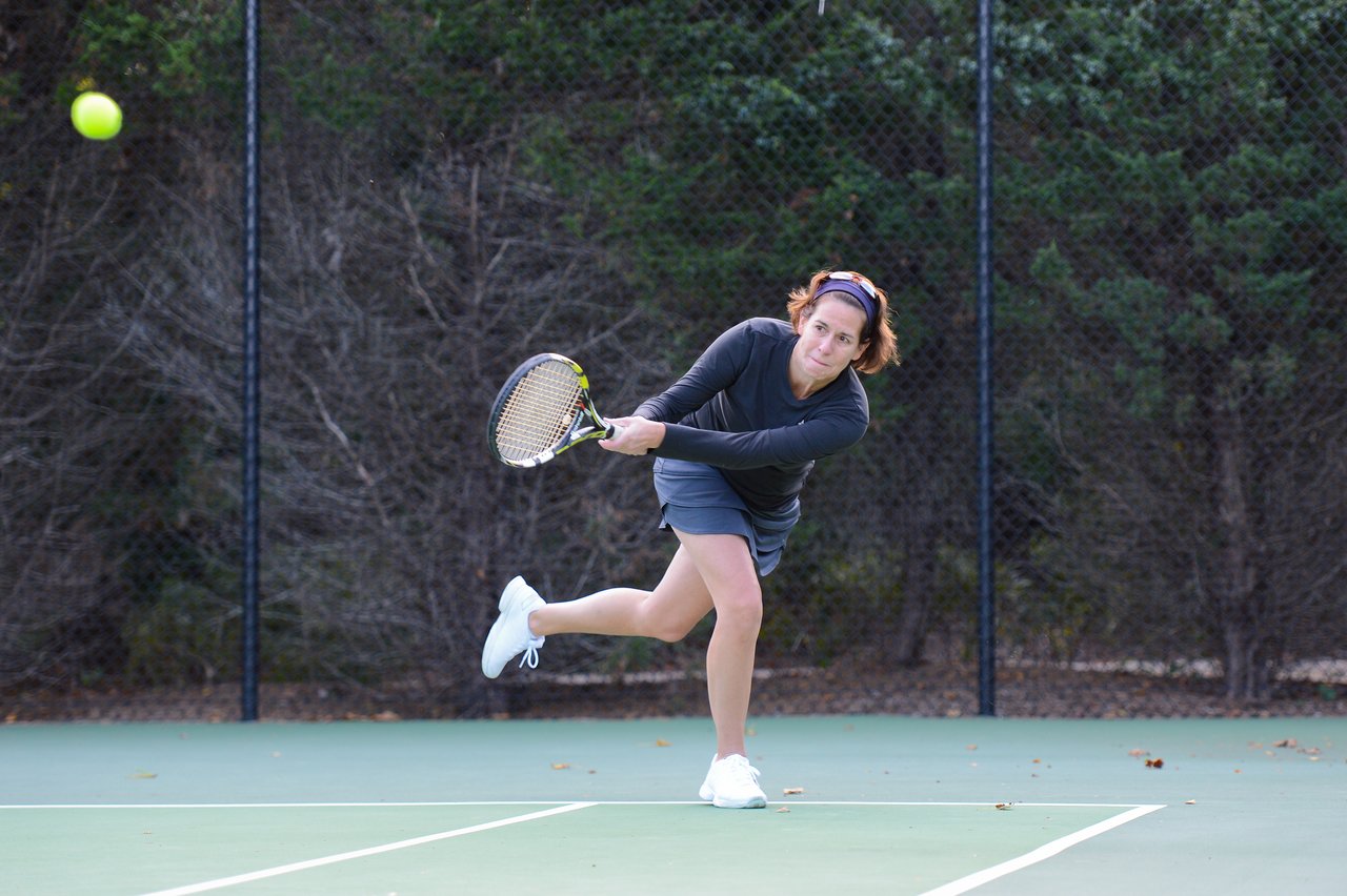 A person plays tennis, swinging a racket to hit the ball on an outdoor court.