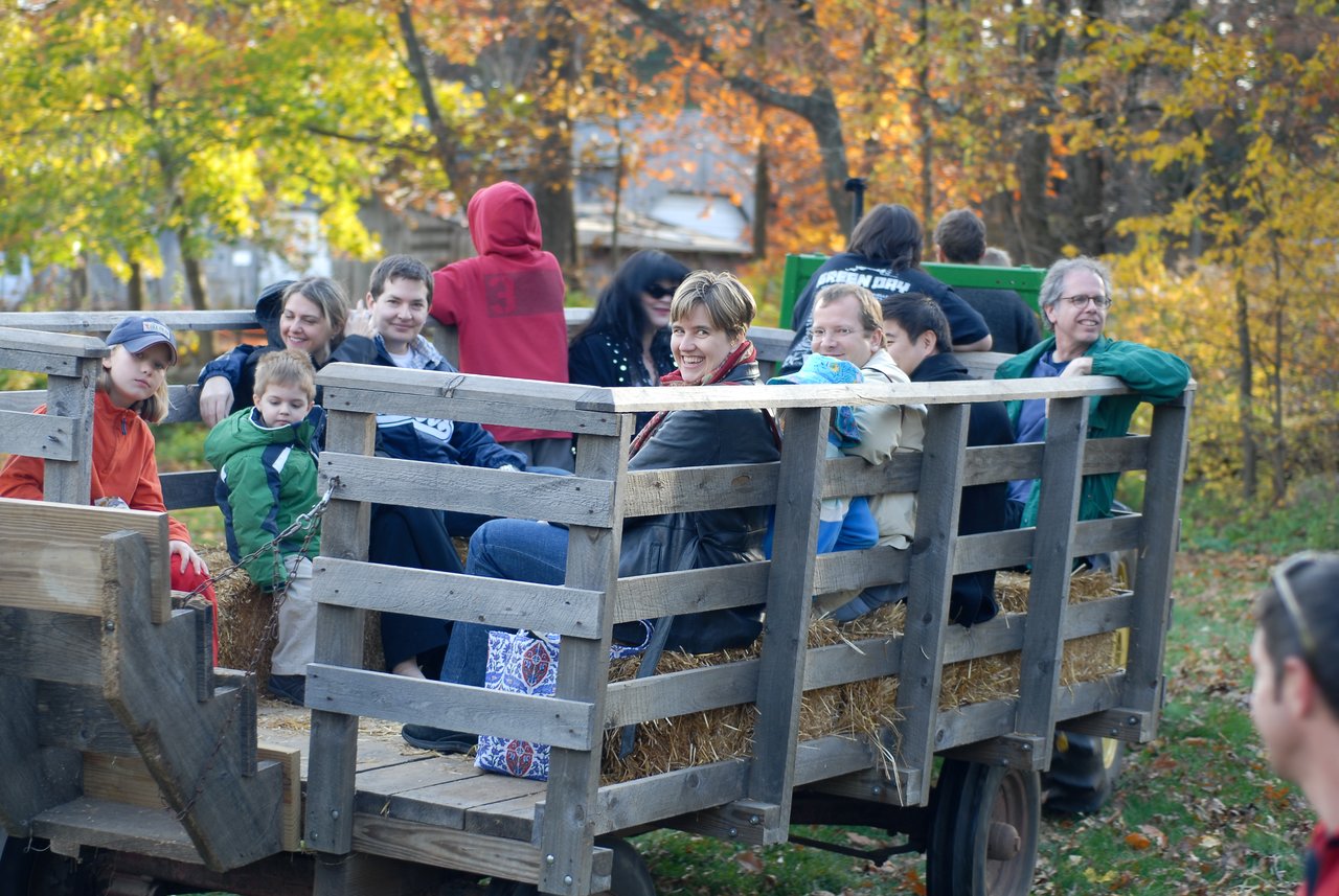 A group of people sit on hay bales in a wooden wagon during a hayride, smiling and enjoying the ride.
