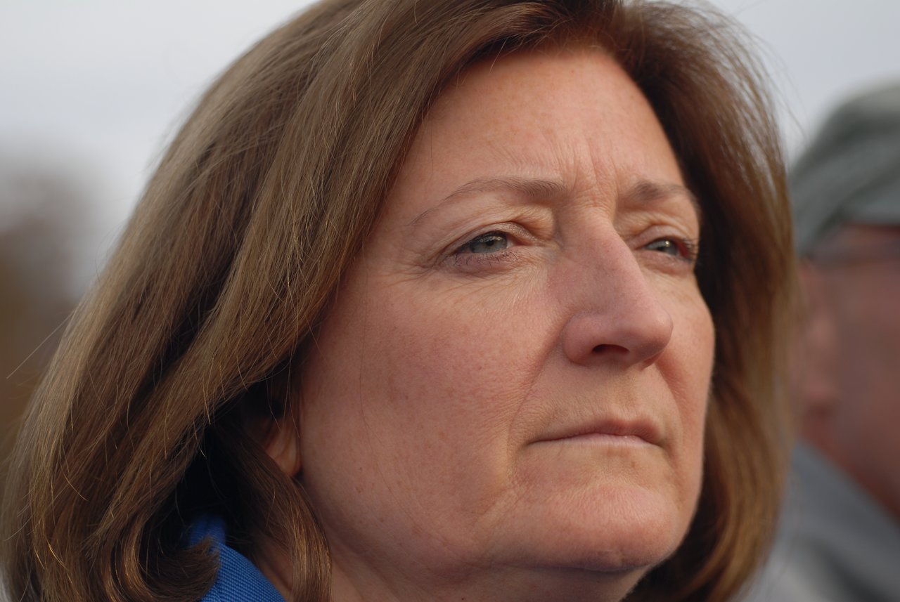 A woman with shoulder-length brown hair looks into the distance with a serious expression.