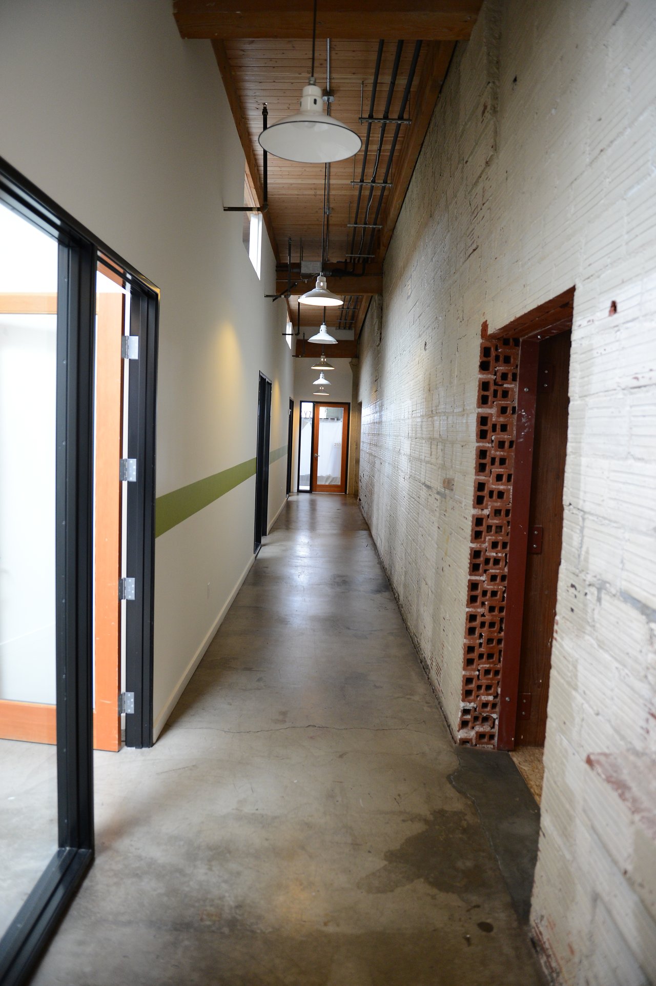 A long hallway in the Acquia Portland office with exposed brick, glass doors, and hanging ceiling lights.