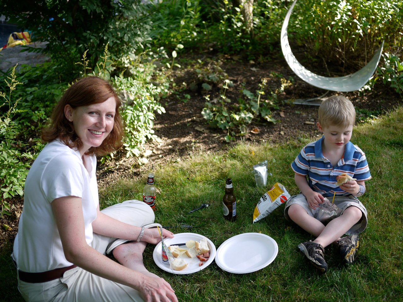 A woman and a young boy sit on the grass, eating food and enjoying a picnic together.
