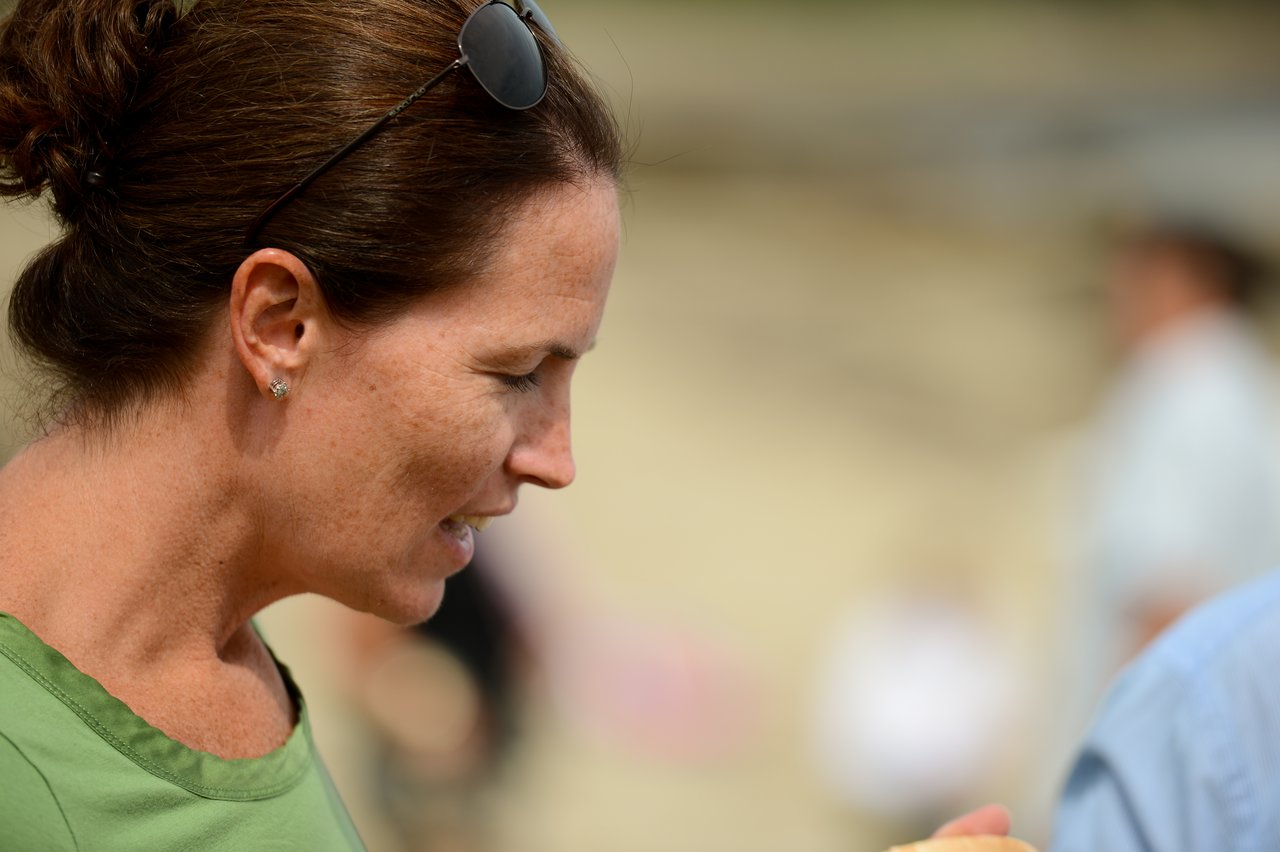 A woman in a green shirt talks to someone at an outdoor gathering, with blurred people in the background.