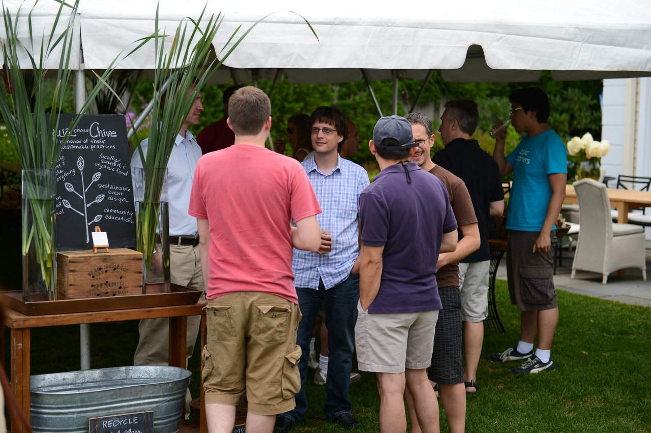 A group of people stand under a tent, talking and socializing at an outdoor party.