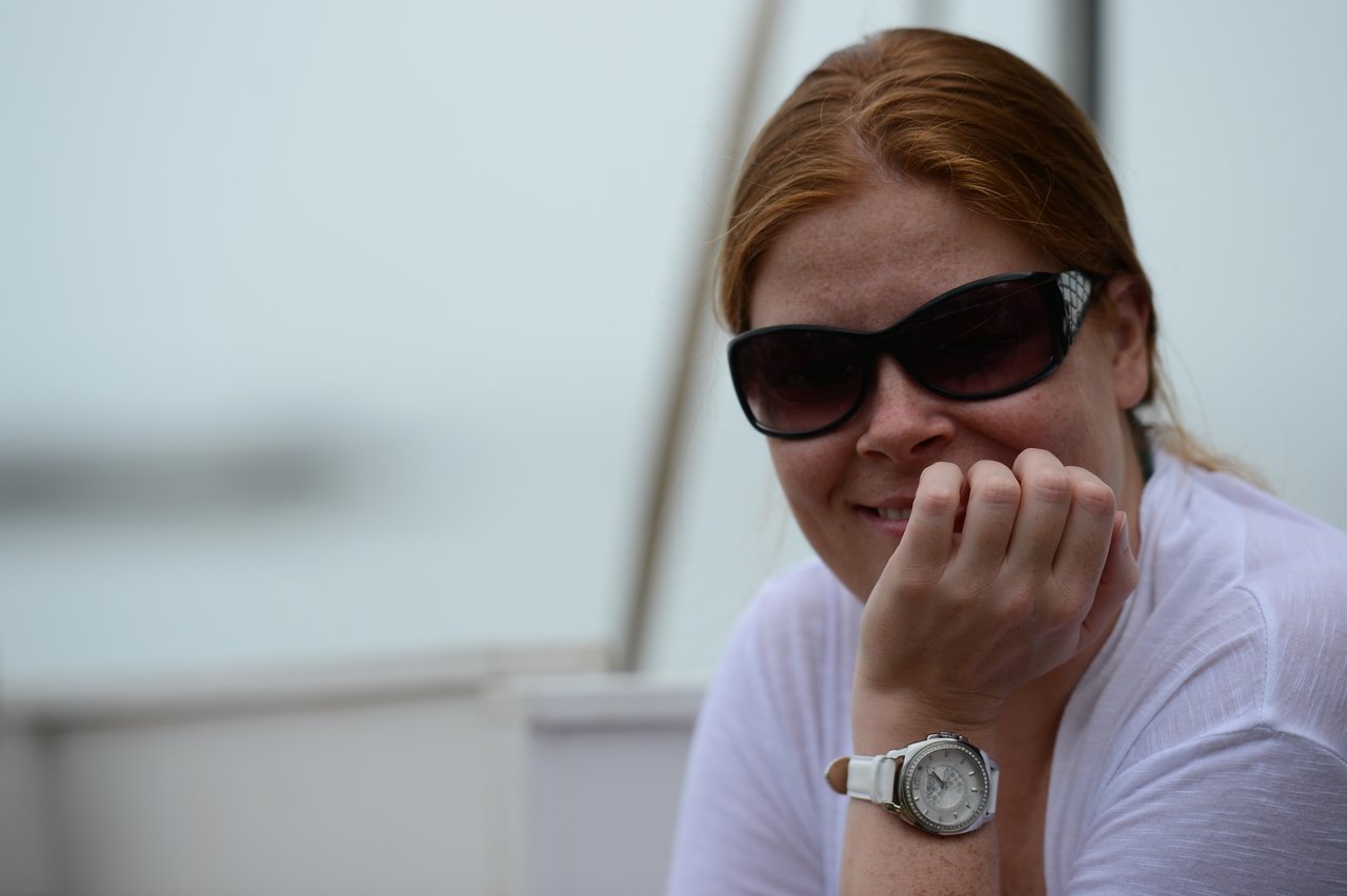 A woman wearing sunglasses and a white shirt smiles while resting her chin on her hand.