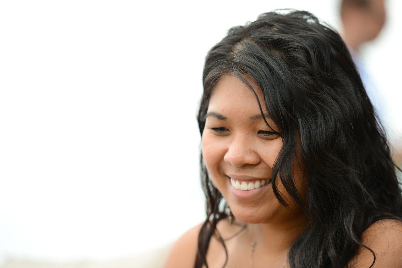 A woman with long, wavy hair smiles while looking down at something during a party.