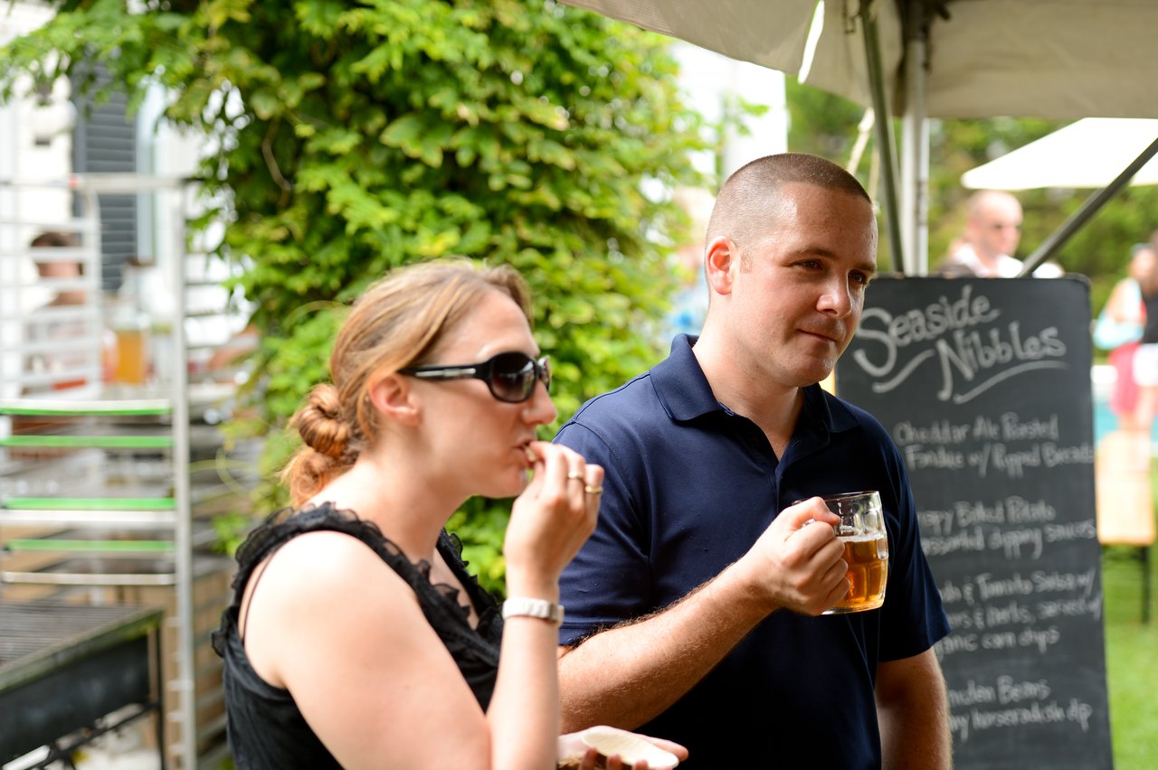 A woman and a man enjoy food and drinks at an outdoor party under a tent.