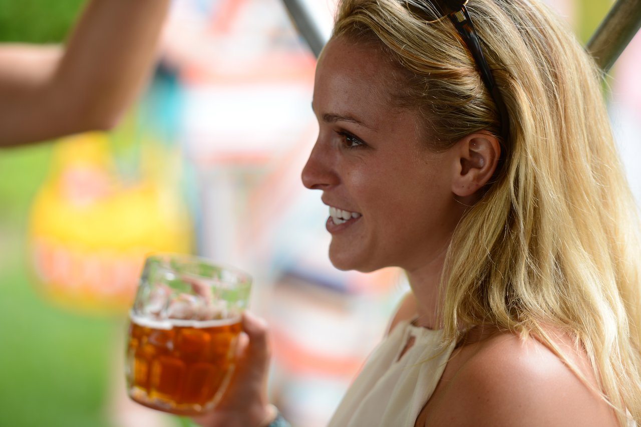 A smiling woman with blonde hair holds a glass of beer while talking at an outdoor party.