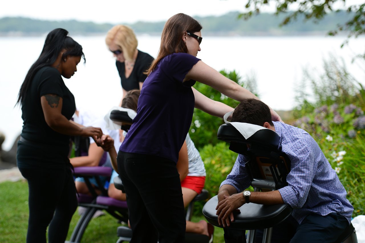People receiving chair massages outdoors, with massage therapists providing relaxation at a summer party.