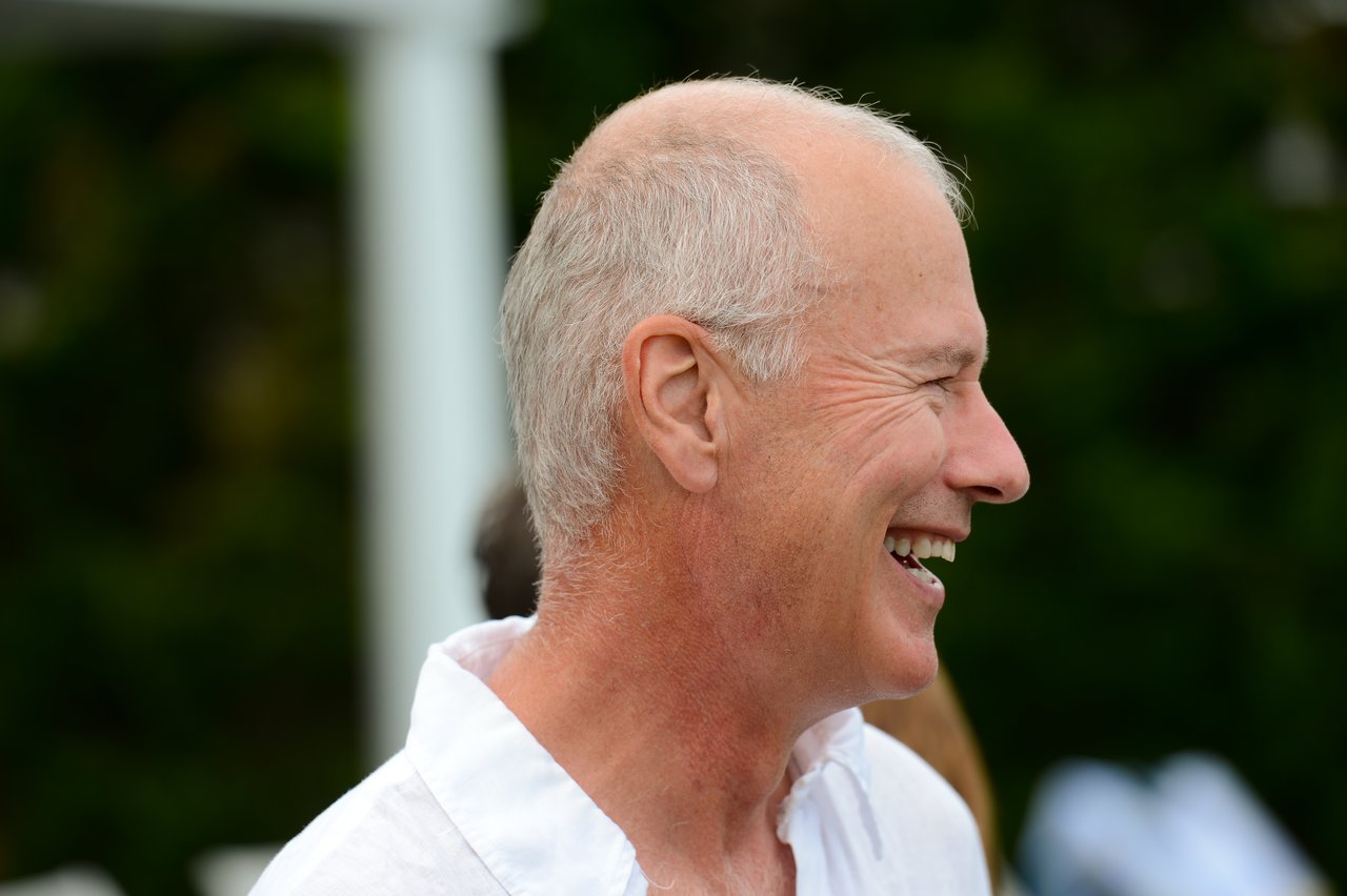 A man in a white shirt laughing at an outdoor summer party.