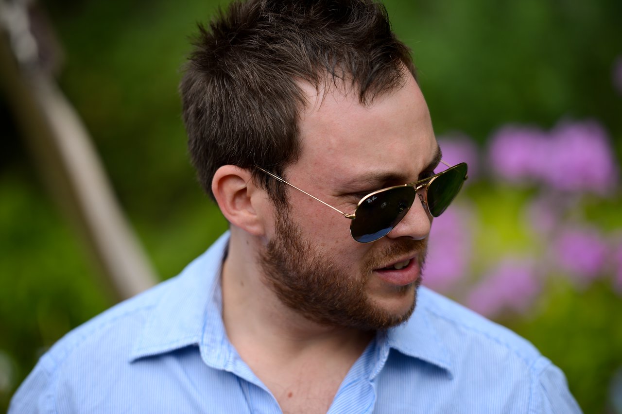 A man in sunglasses and a blue shirt looks to the side at an outdoor gathering.