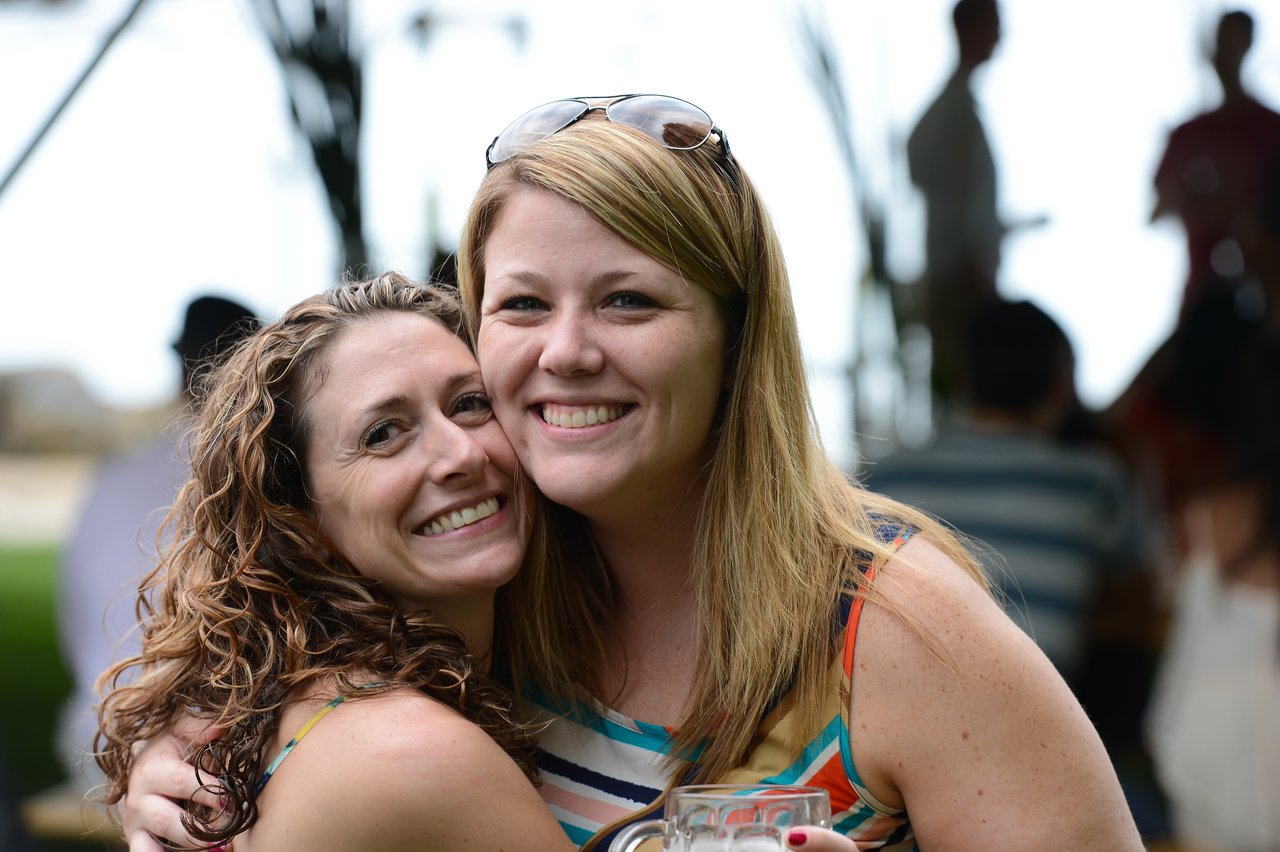 Two smiling women pose closely together at an outdoor party, one holding a drink.