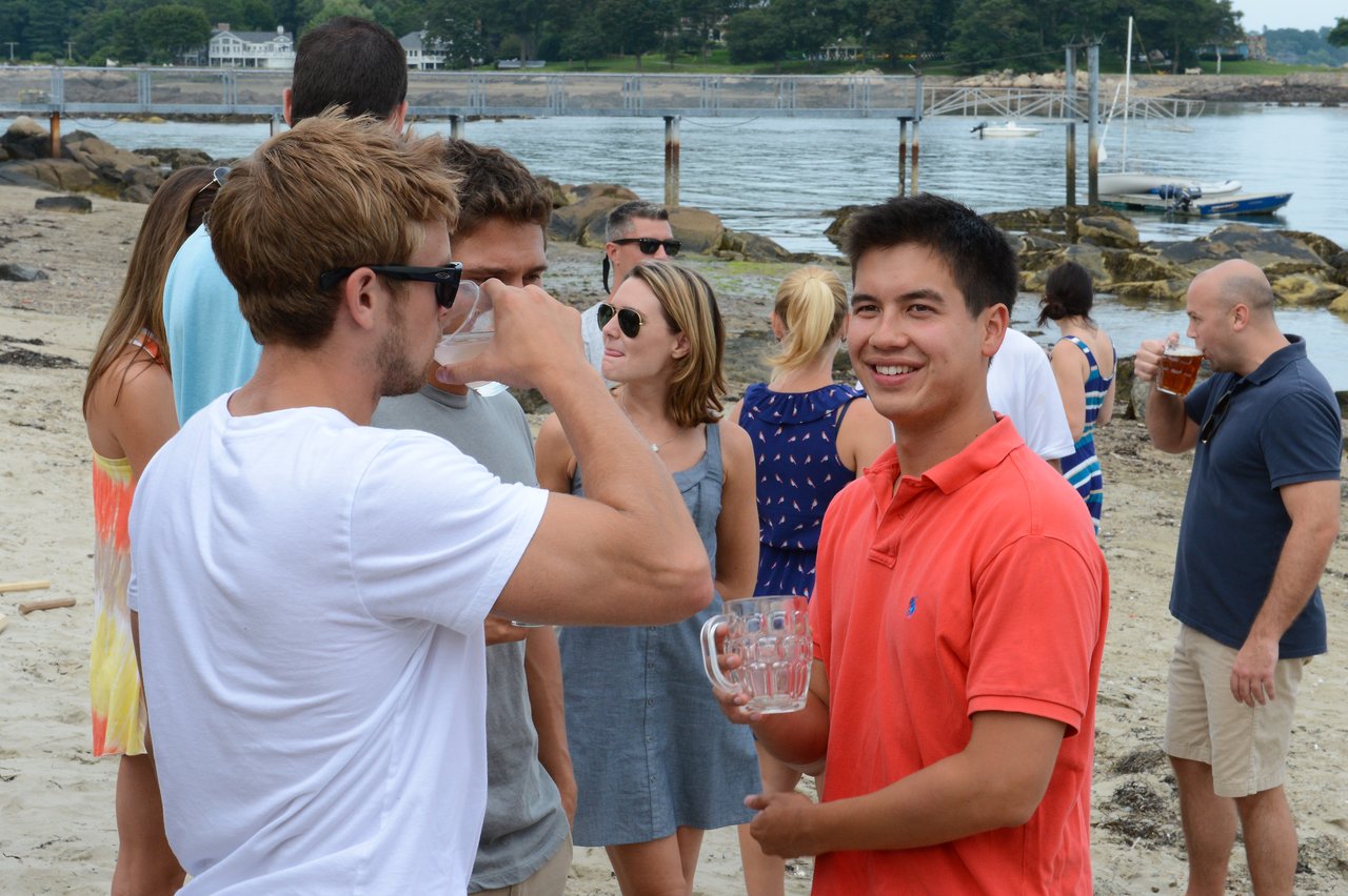 People socializing on a beach, holding drinks and chatting.
