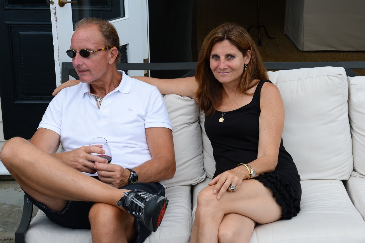 A man and woman sit on a white outdoor couch, relaxing.