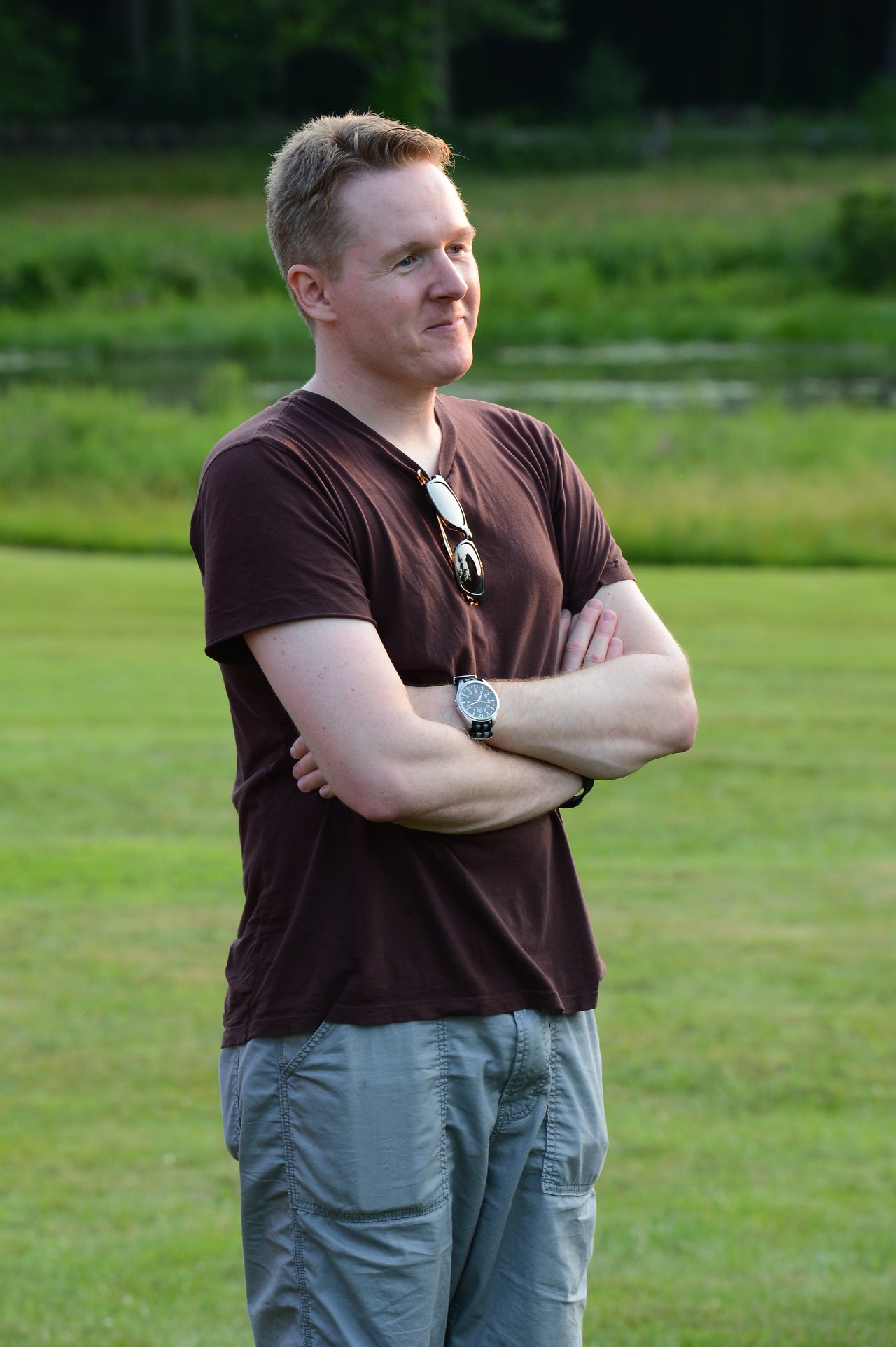A man stands on the grass with arms crossed, watching the dunk tank event at the summer party.