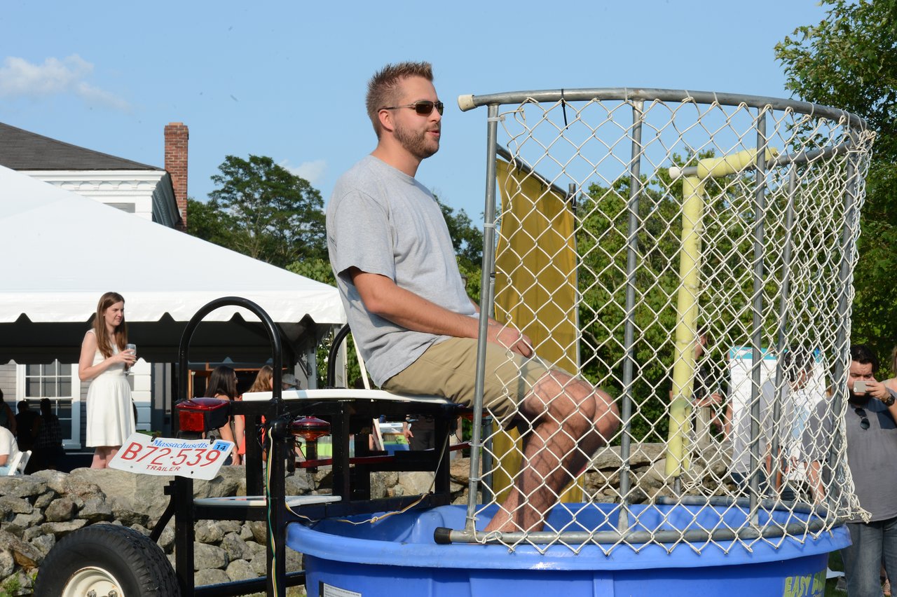 A man sits on a dunk tank platform, waiting to be dropped into the water at an outdoor event.